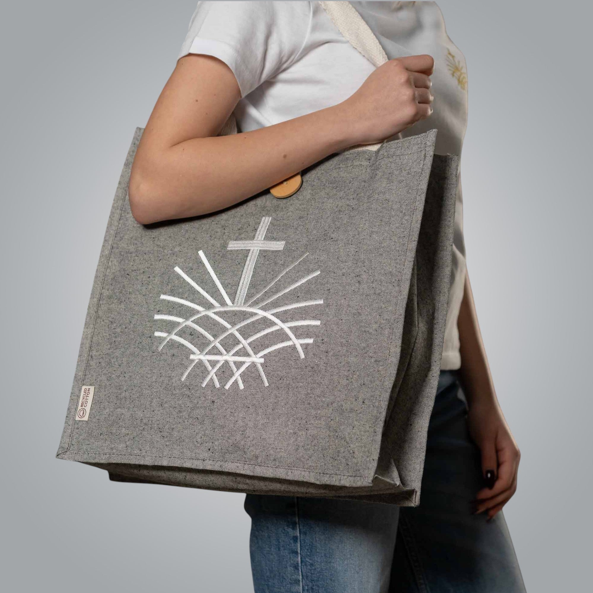 Grey tote bag with white embroidered Christian Loom in Light emblem carried by woman