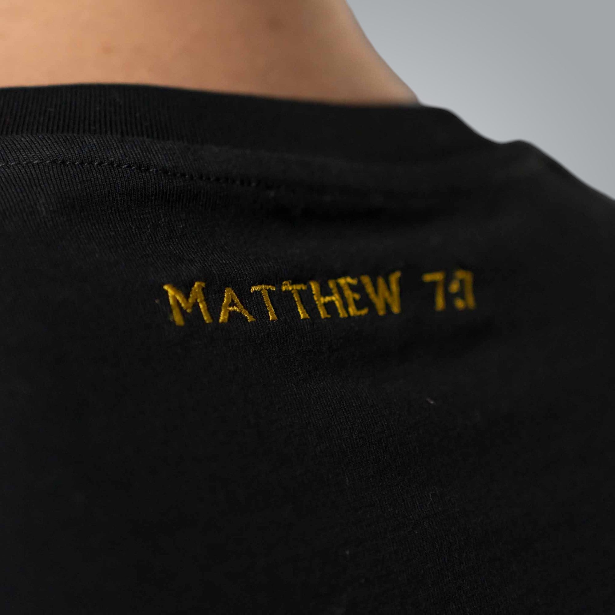 Close up of gold embroidered Matthew 7:7 text on black men’s Christian t shirt