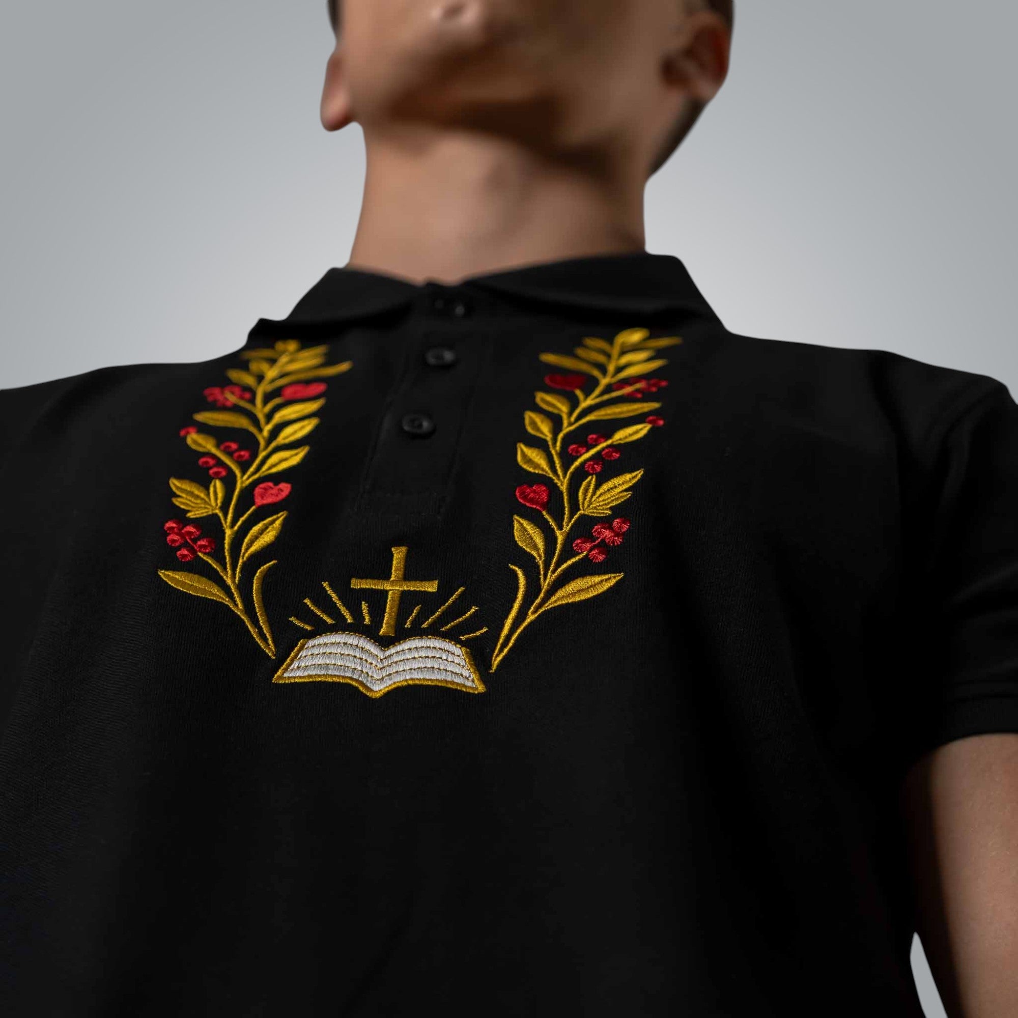 Close up of embroidered cross open Bible and branches on black men’s Christian polo