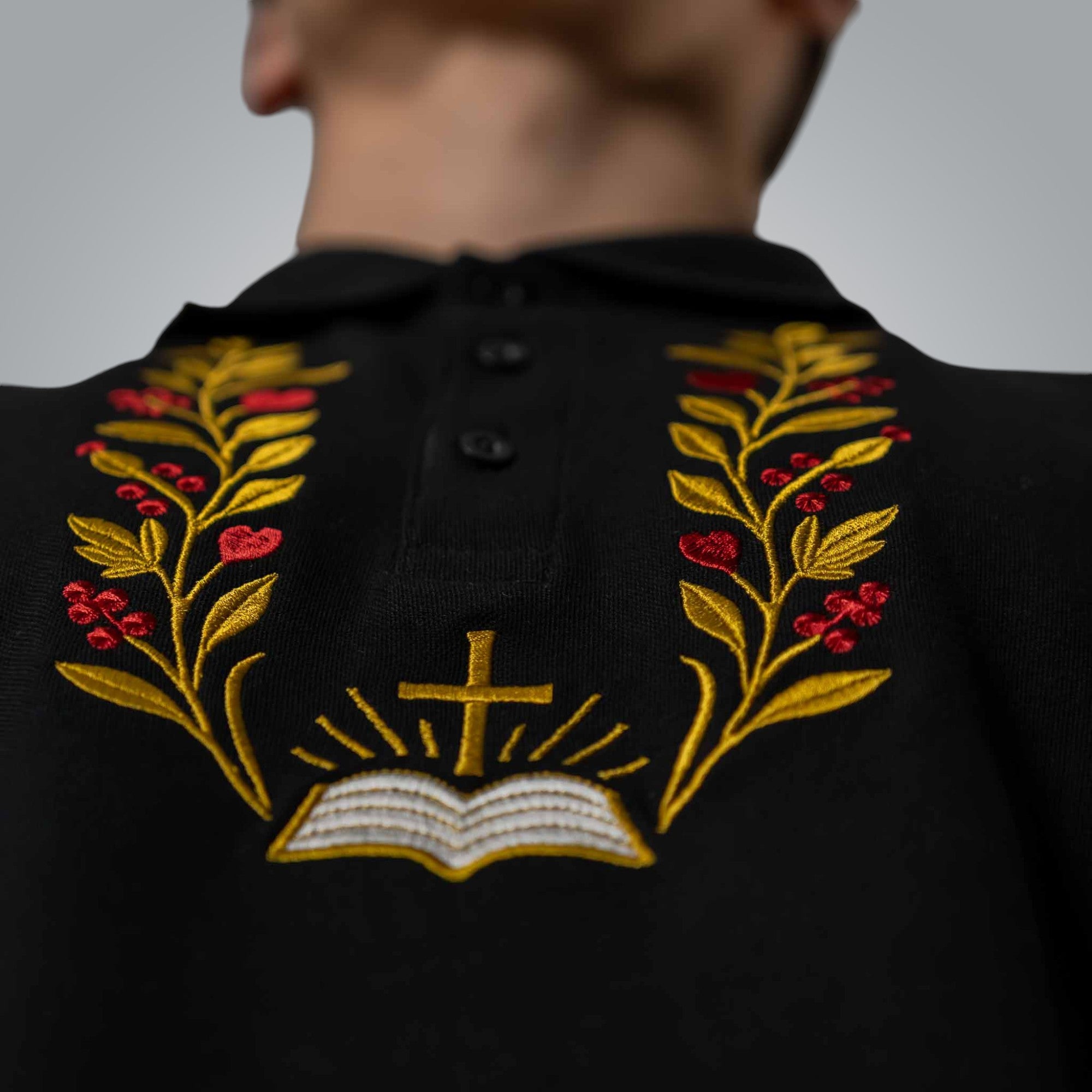 Macro detail of red and gold embroidery of branches and Bible on black Christian polo