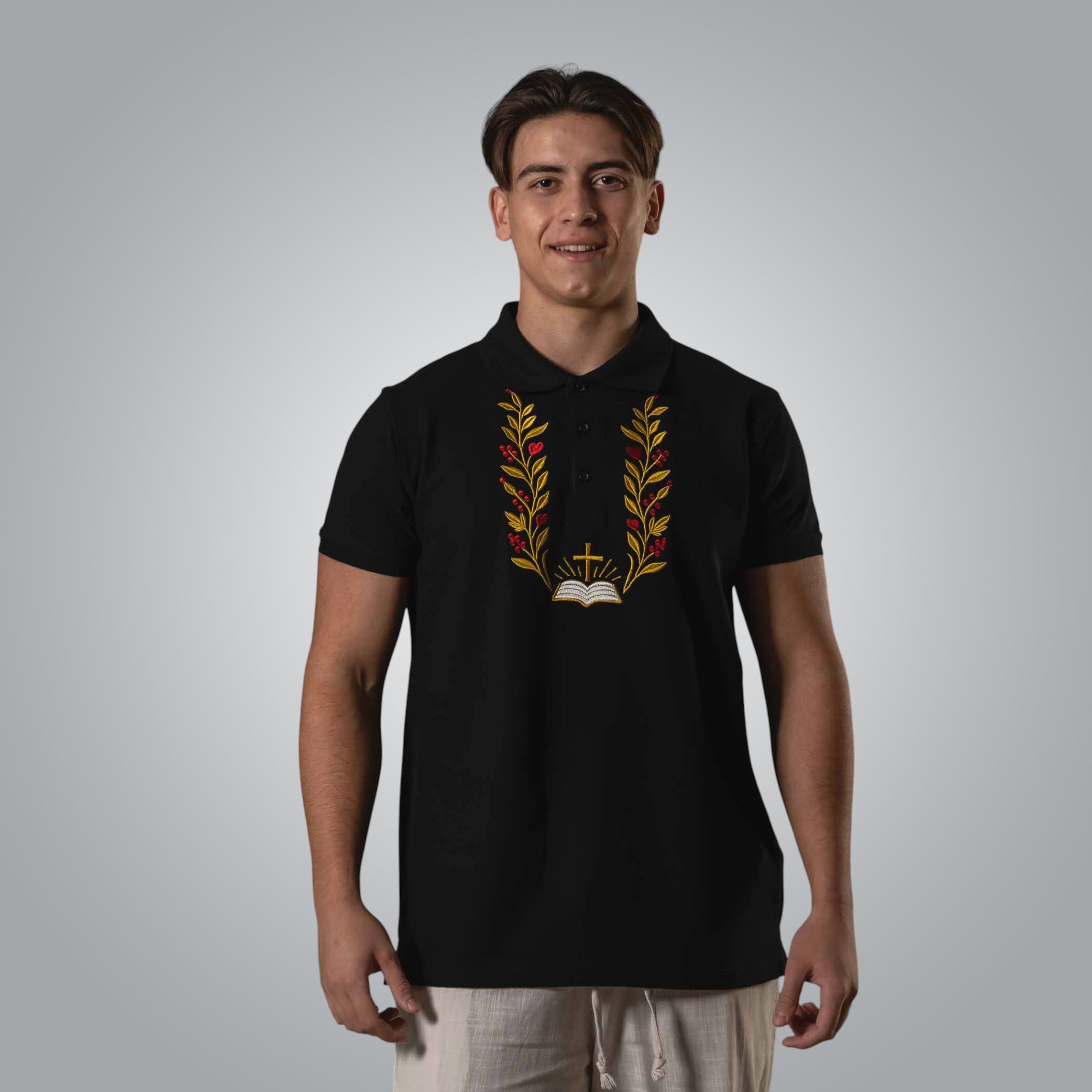 Full body view of man wearing black Christian polo with gold and red embroidery inspired by John 1:1