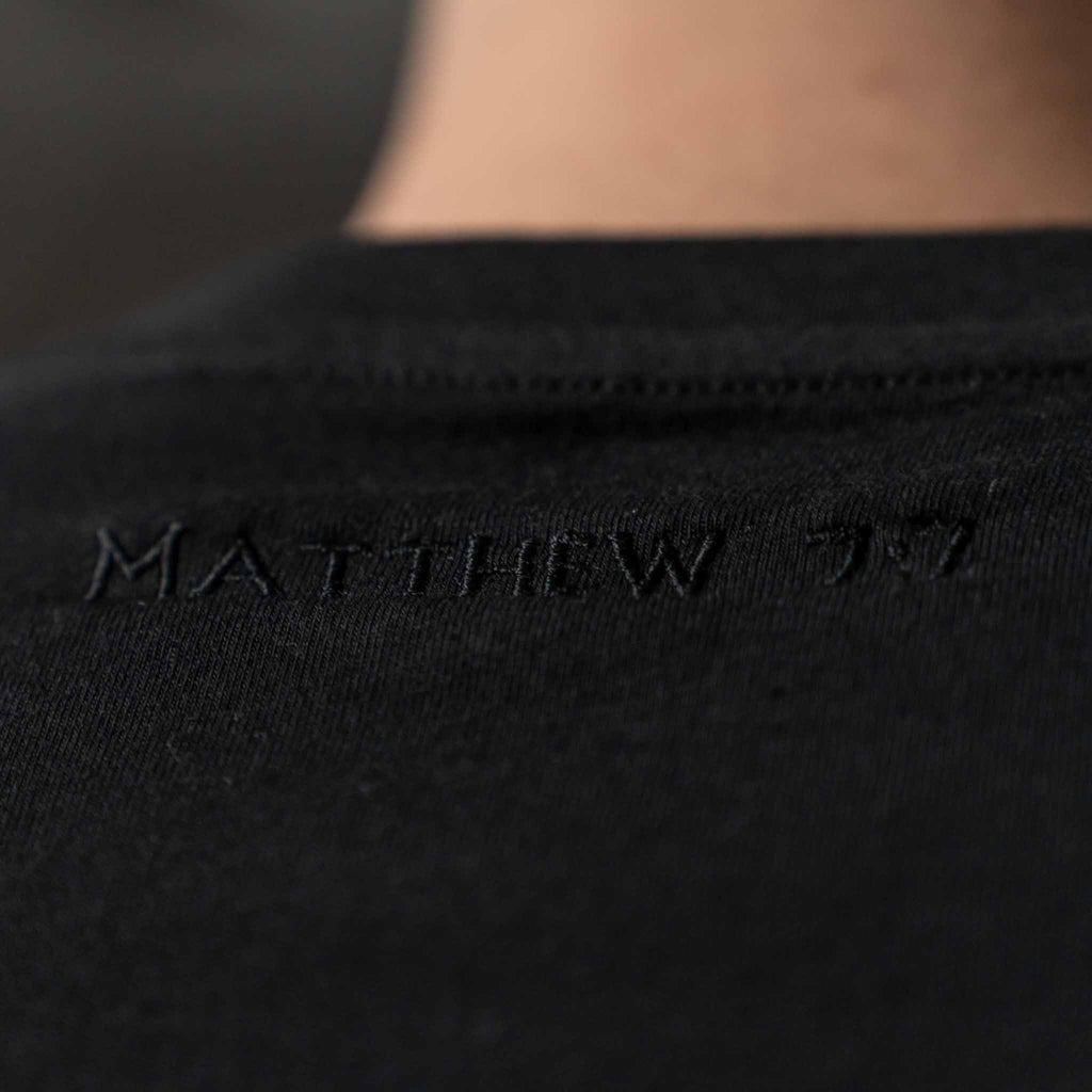 Close up of black embroidered Matthew 7:7 text on the back of black men’s Christian t shirt
