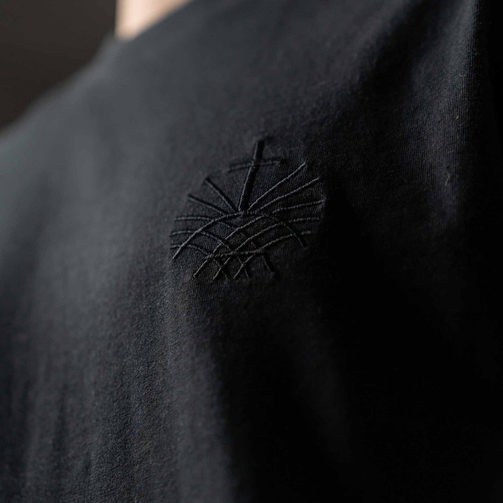 Close up of black embroidered Loom in Light emblem on black men’s t shirt
