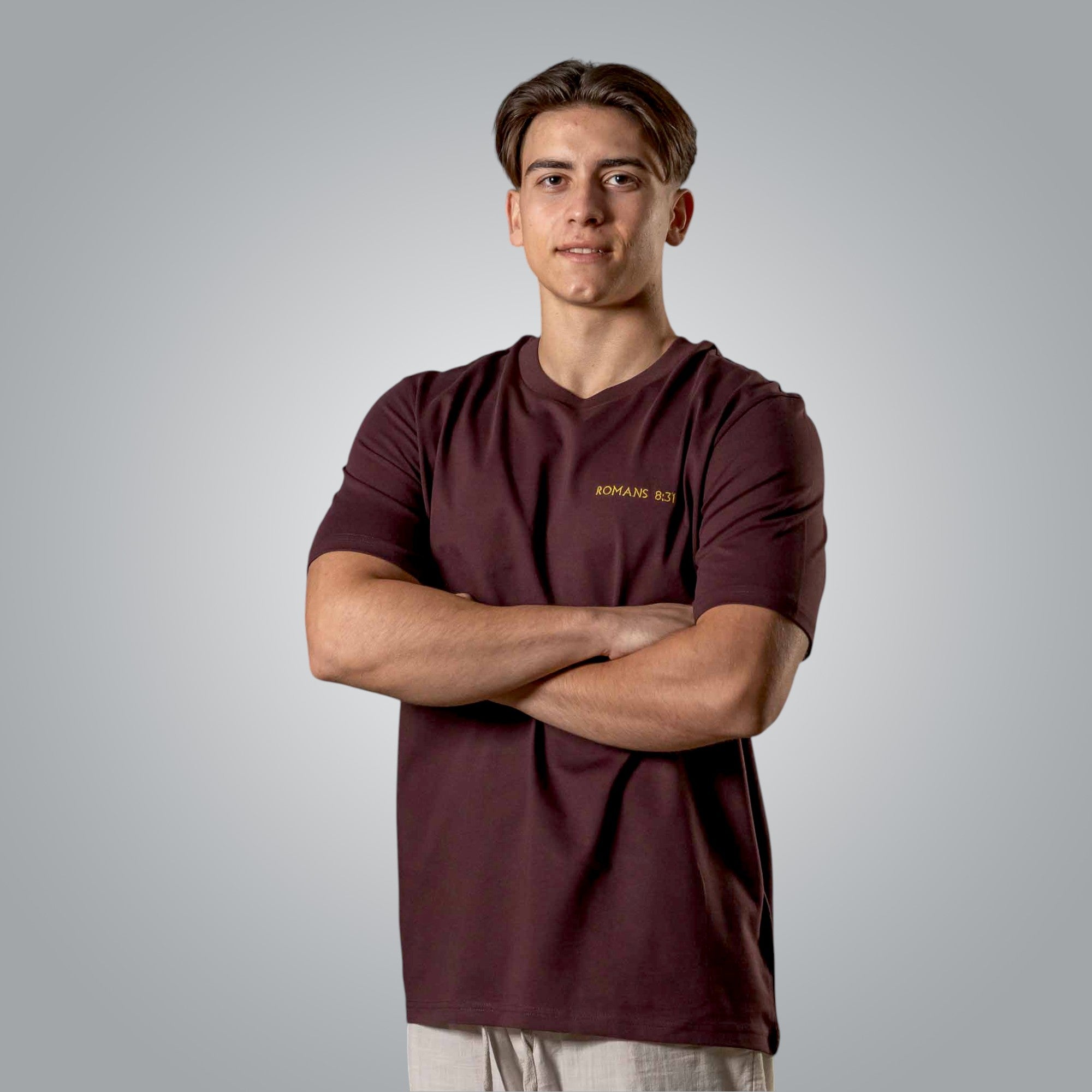 Front view of man in burgundy t shirt with gold embroidered Romans 8:31 verse on the chest