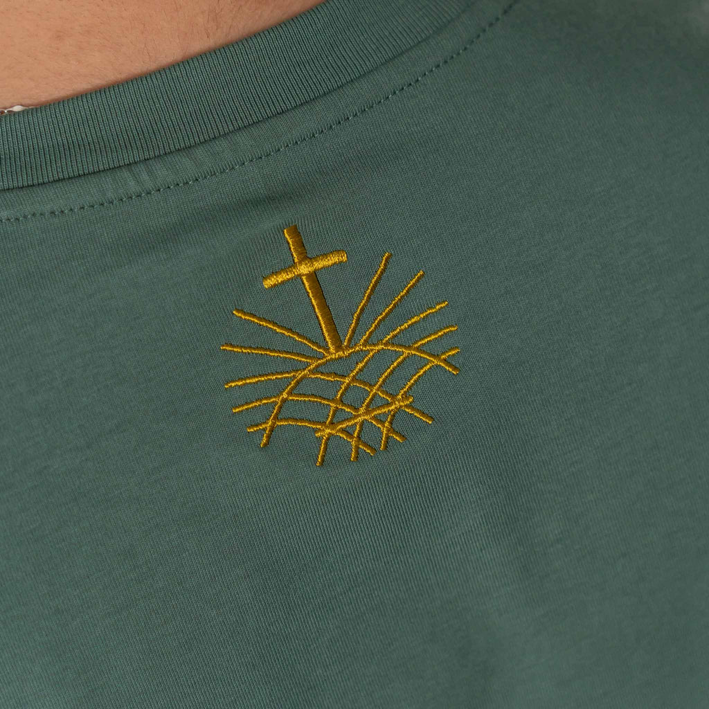 Close up of gold embroidered Loom in Light logo on green Christian t shirt