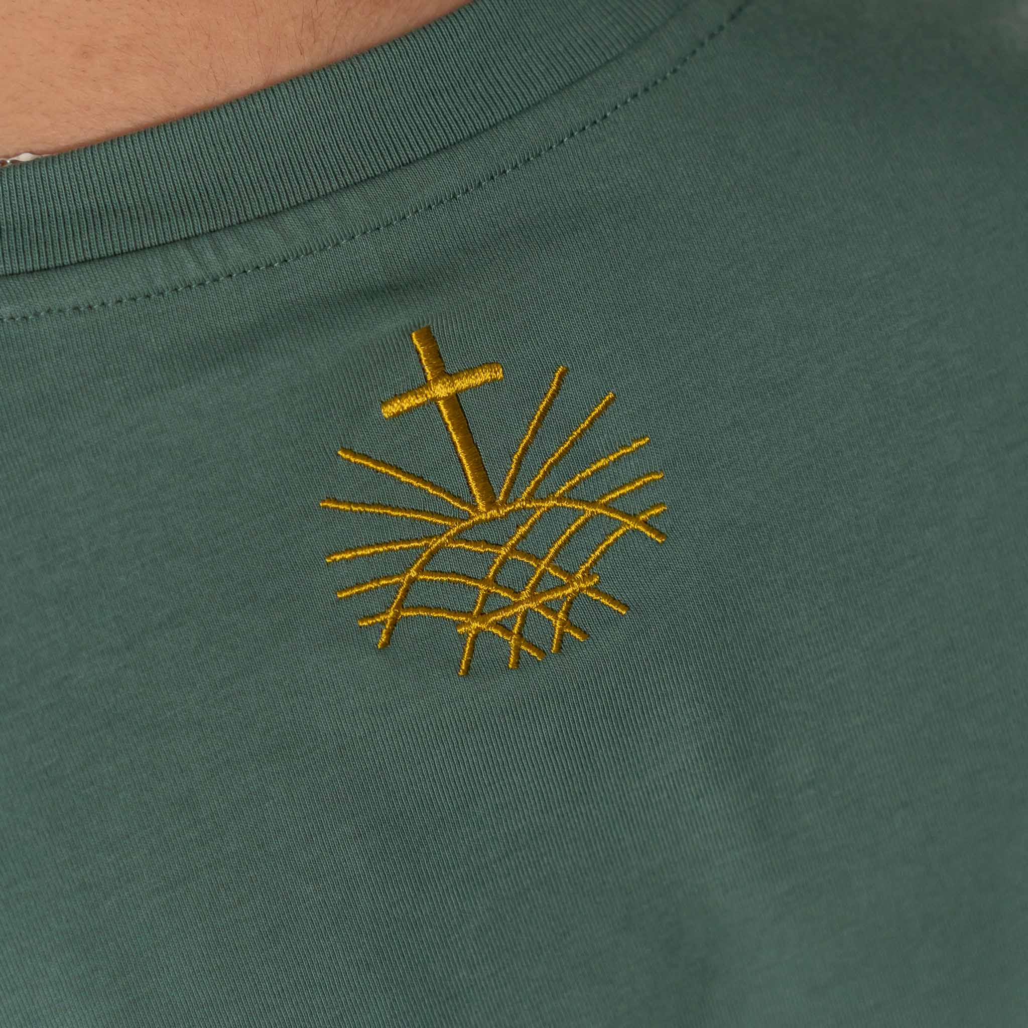 Close up of gold embroidered Loom in Light logo on green Christian t shirt
