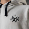 Close up of black embroidered Loom in Light cross emblem on men’s white hoodie