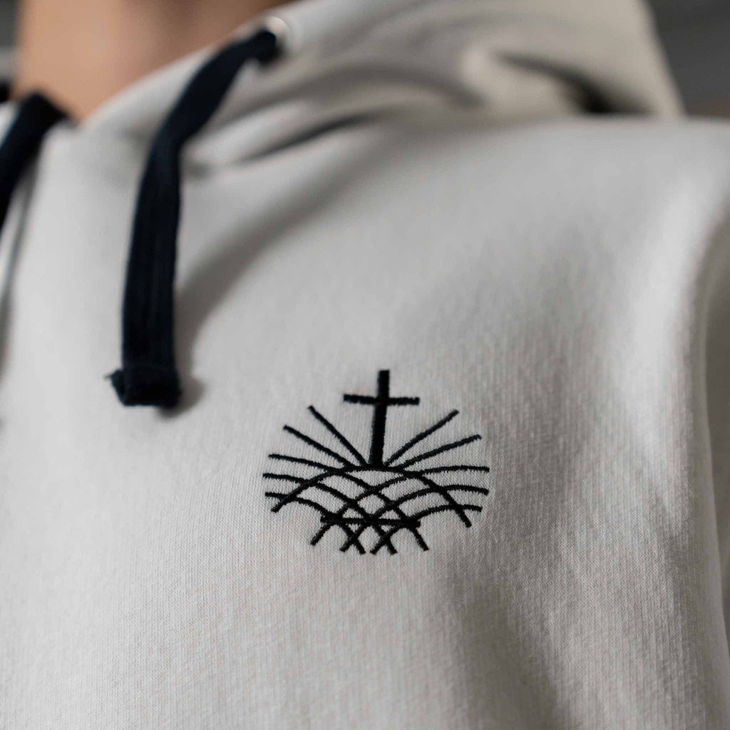 Close up of black embroidered Loom in Light cross emblem on men’s white hoodie