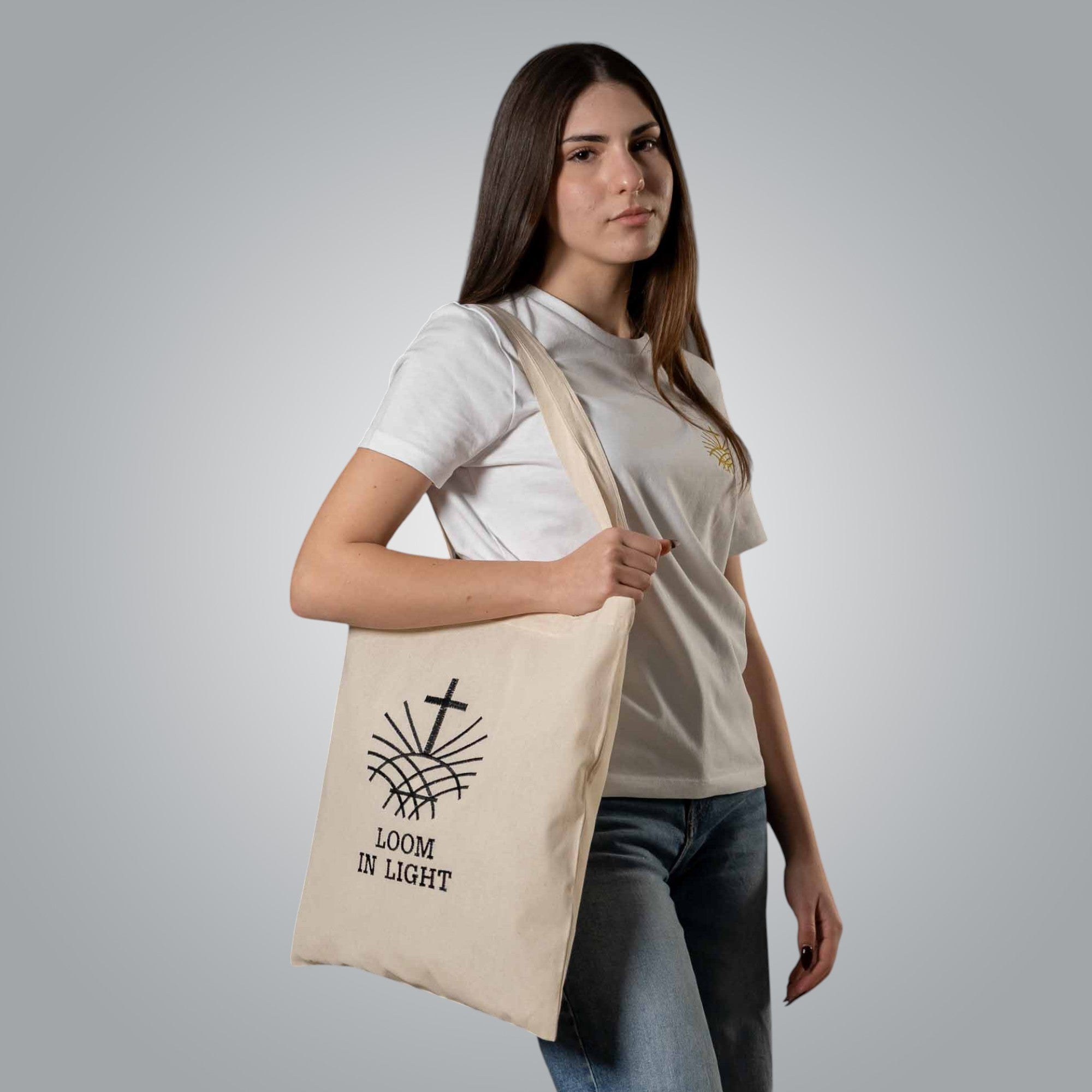 Woman carrying natural cotton tote bag with black embroidered Loom in Light logo