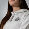 Close up of black embroidered Loom in Light cross emblem on white women’s hoodie