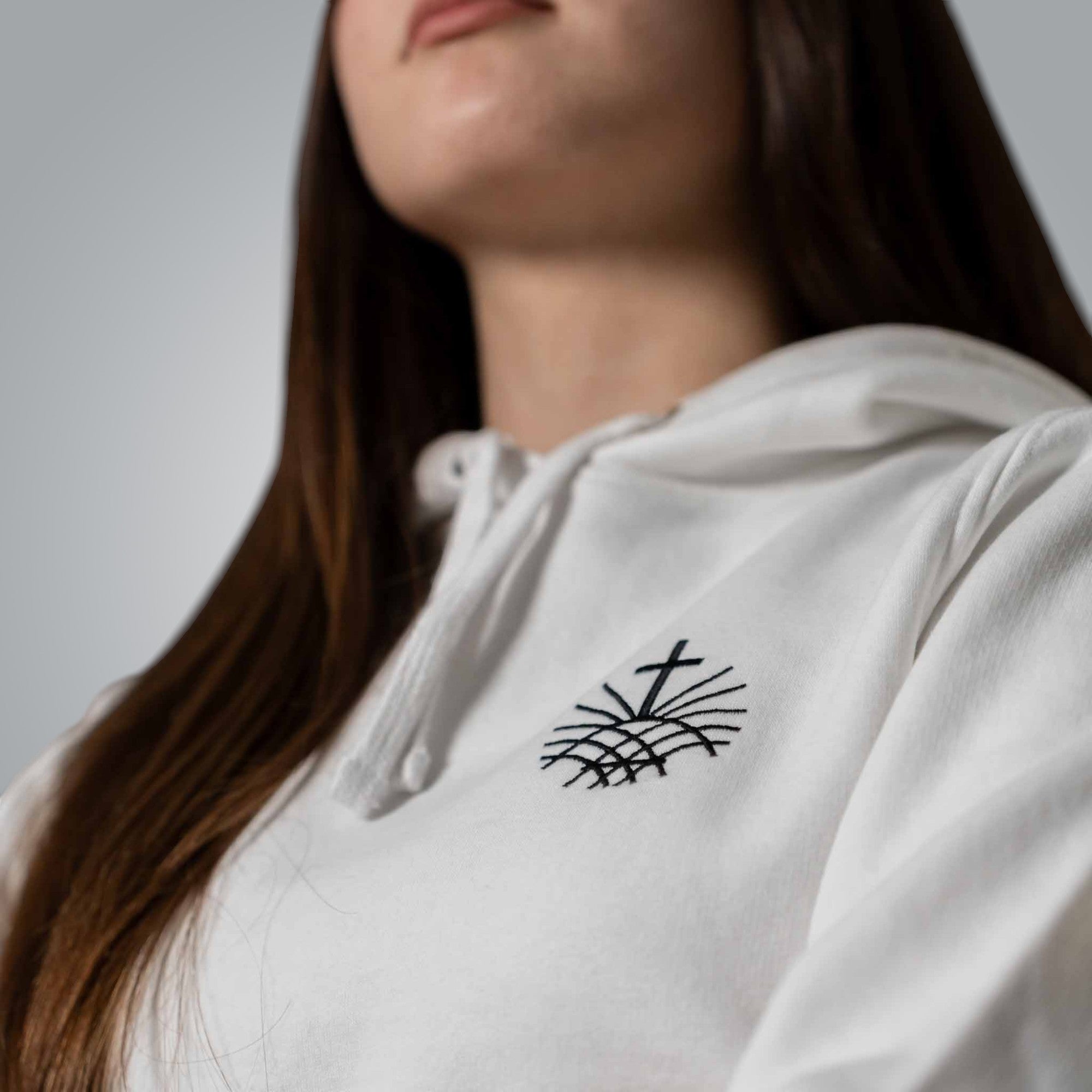 Close up of black embroidered Loom in Light cross emblem on white women’s hoodie