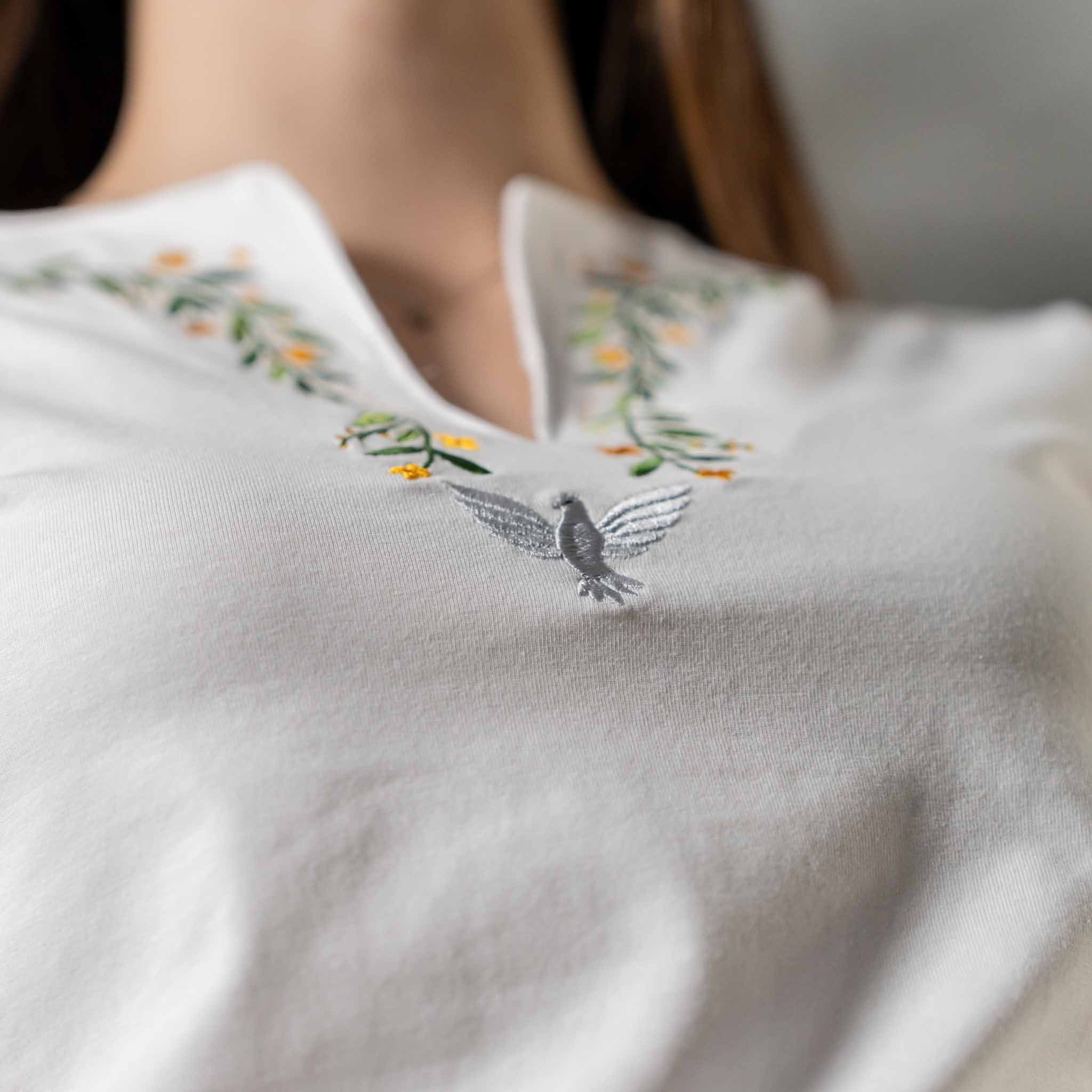 Macro close up of embroidered dove and floral design on white Christian V neck t shirt